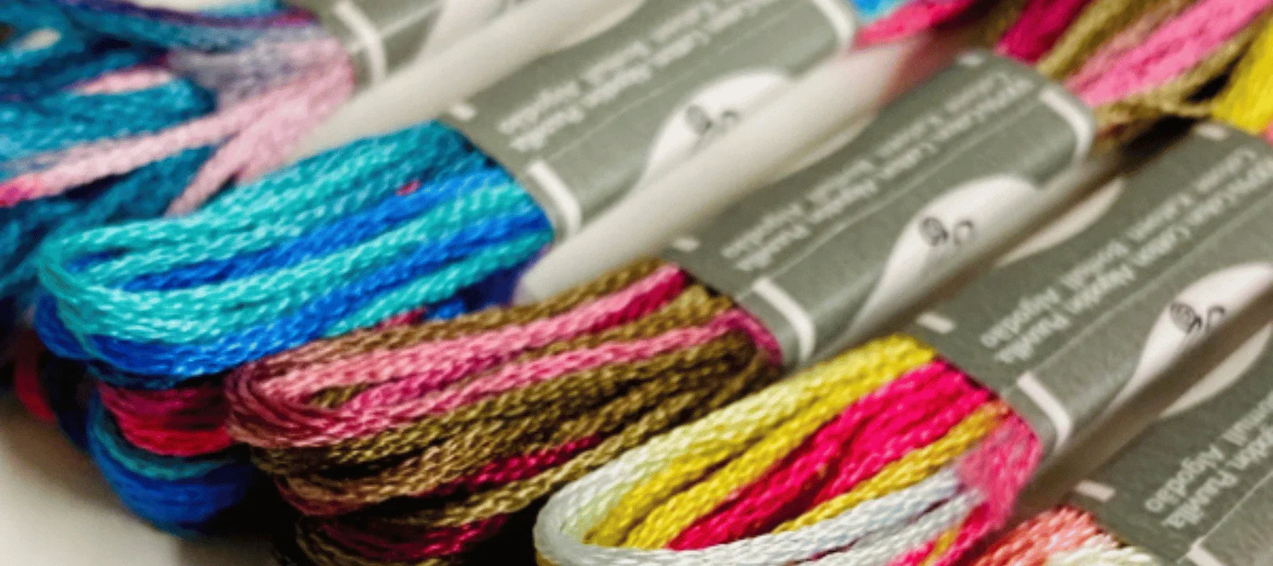 Close-up of several skeins of colorful embroidery floss, including shades of blue, pink, brown, and yellow, bundled together with gray paper labels.