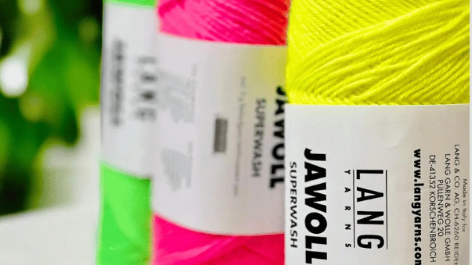 Three skeins of LANG YARNS JAWOLL Superwash yarn in neon green, pink, and yellow are lined up in a row, with the labels clearly visible in the foreground.