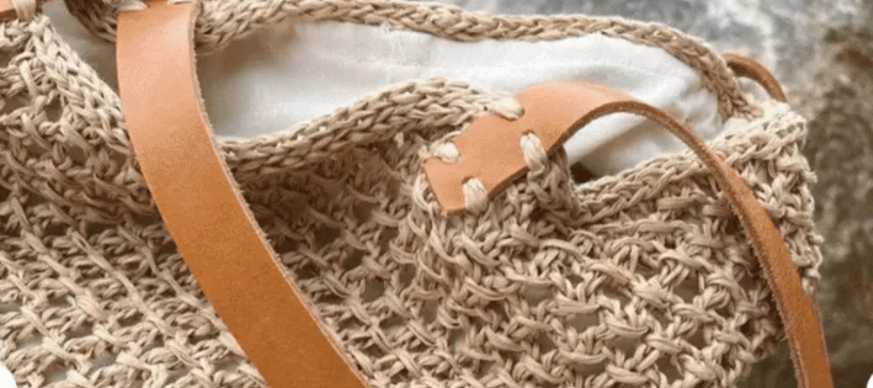 A close-up of a woven beige handbag with a tan leather strap and white fabric lining inside. The bag features a textured, crochet-style pattern.