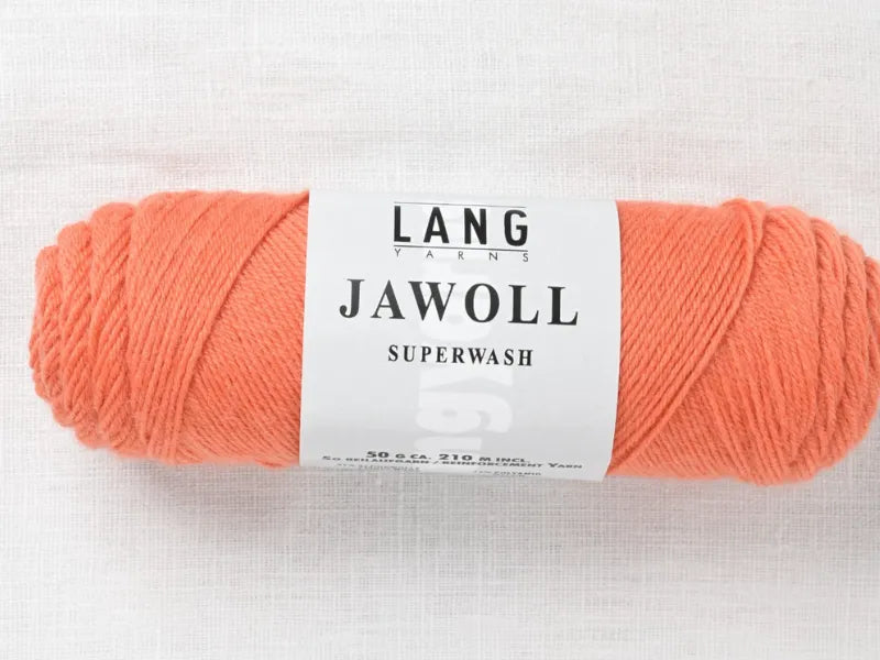 A skein of Timo sukka ohje fingerin ja Lang jawoll yarn is displayed on a white textured surface, with its label visible and wrapped around the coral-colored skein.