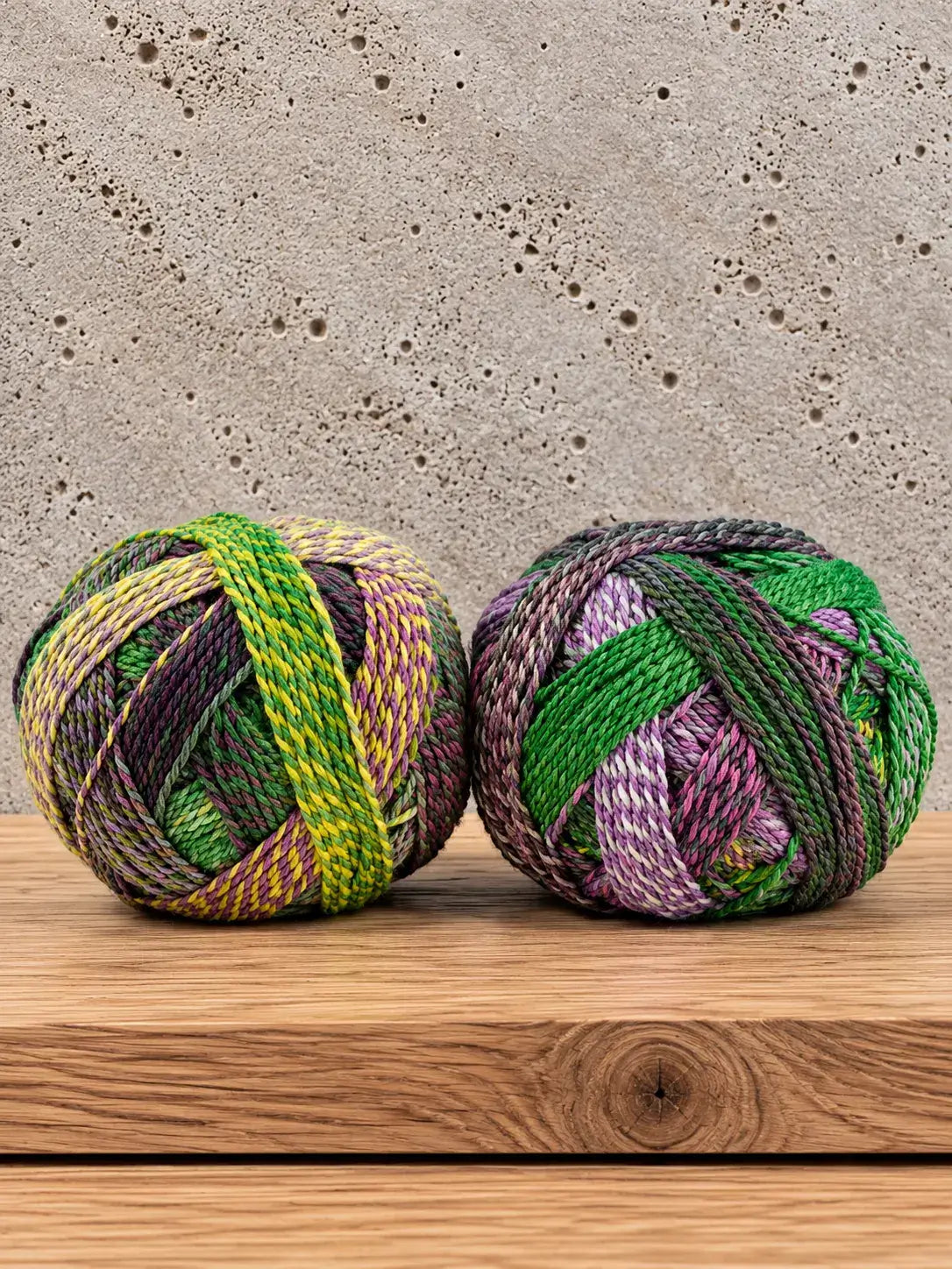 Two balls of Schoppel-Wolle Edition 3 variegated yarn in shades of green, purple, and yellow sitting on a wooden surface.