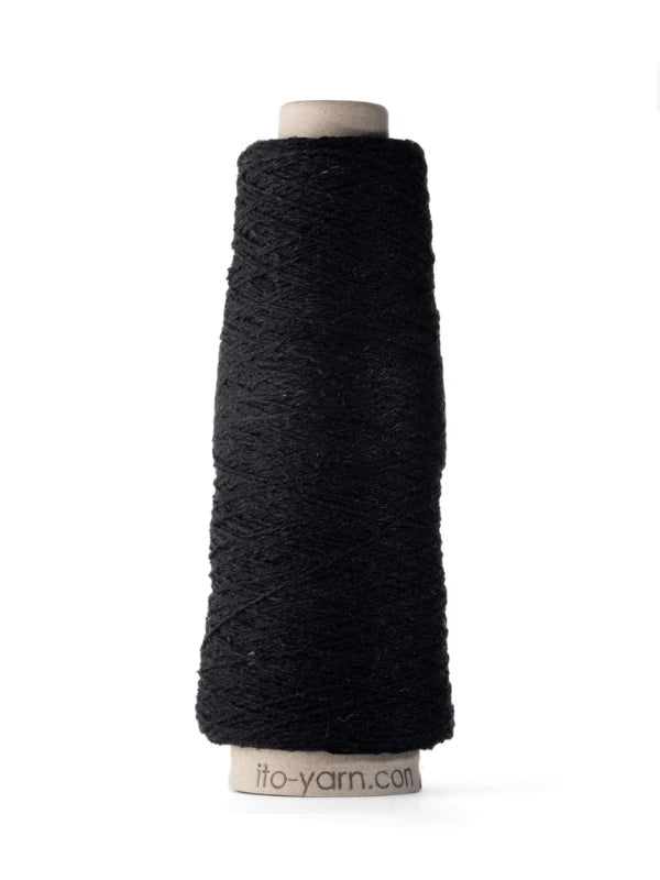 A cone of Ito Kinu black silk yarn with a textured surface, wound around a cylindrical cardboard spool marked ito-yarn.com. This 100% silkki is perfect for kesäneuleisiin, shown against a clean white background.