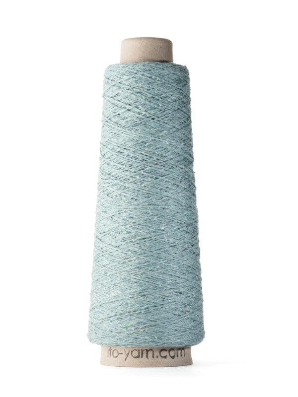 A cone of light blue Ito Kinu, 100% silk, is wound on a cardboard spool and stands upright on a white background. Faint text is partly visible at the bottom edge—ideal for kesäneuleisiin.