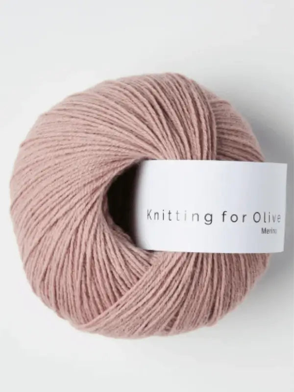 A ball of soft, dusty pink Knitting for Olive Merino yarn with a white label is displayed against a plain light background.