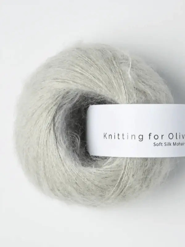 A light gray ball of Knitting for Olive Soft Silk Mohair yarn, blended with Kid mohair and silk and featuring a white label that reads "Knitting for Olive." The yarn looks fluffy and delicate, ideal for knitting or crocheting projects, reflecting the luxurious quality of their Soft Silk Mohair range.