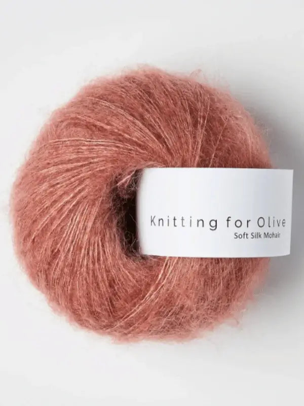 A soft, fluffy ball of Knitting for Olive Soft Silk Mohair in dusty rose, with a white label, rests on a light gray background; this yarn is crafted according to the Responsible Mohair Standard.