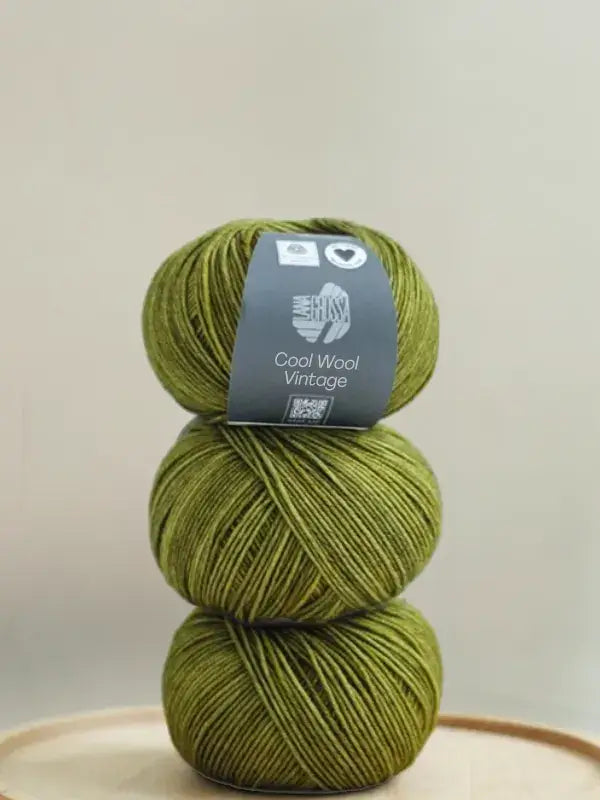 A vertical stack of three balls of olive green Lana Grossa Cool wool vintage yarn.