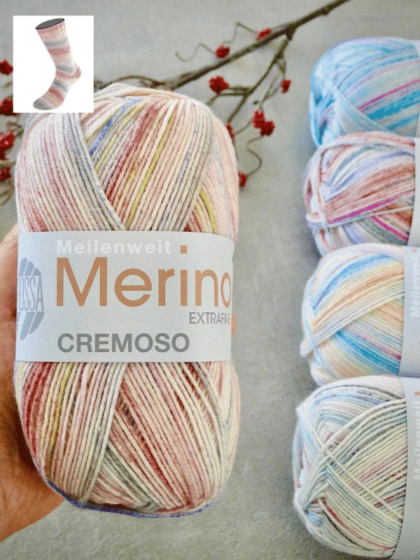 A hand holds a ball of Lana Grossa Meilenweit 100 Merino Extrafine Cremoso. Three similar balls, a branch with red berries, and a sock sample appear in the background. Lanka on konepestävä (machine washable).