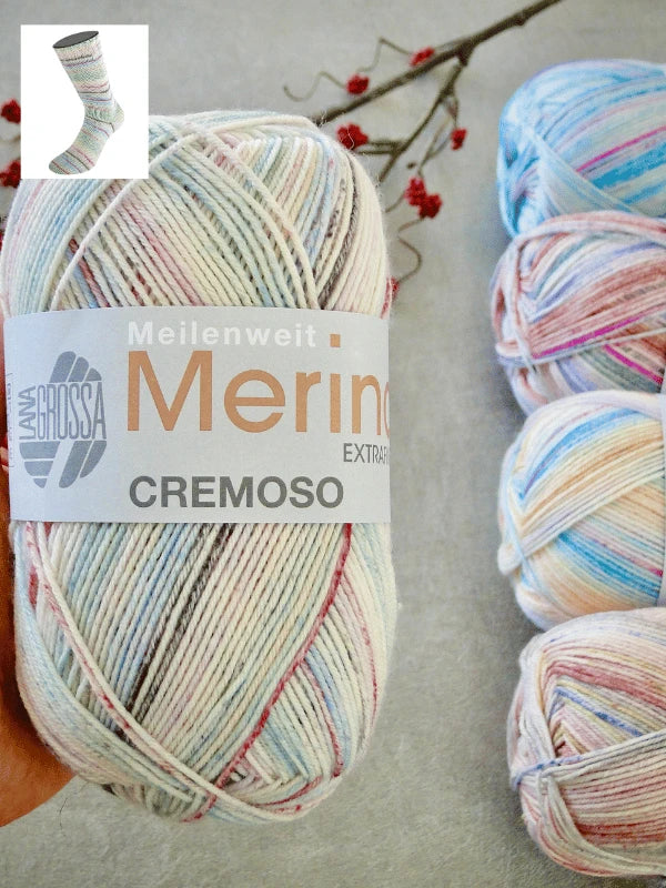 A skein of konepestävä Lana Grossa Meilenweit 100 Merino Extrafine Cremoso pastel-raitasukkalankaa rests on a gray surface with three similar skeins, berry branches, and a small sock preview image in the background.