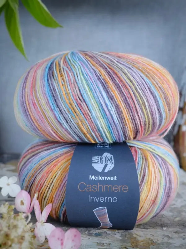 A ball of Lana Grossa Meilenweit 100 Cashmere Inverno yarn, celebrated for its luxurious cashmere blend often favored in premium sukkalanka projects, rests on a surface adorned with small flowers and shaded by green leaves above.