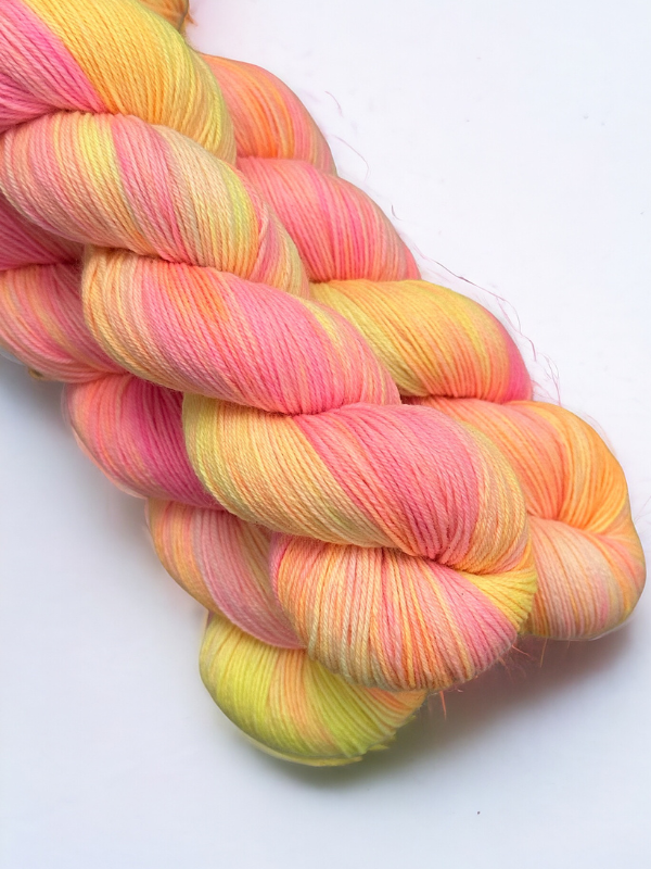A loosely twisted skein of WoolWomen Merino Sock in soft pastel shades of pink, yellow, and orange, set against a white background.