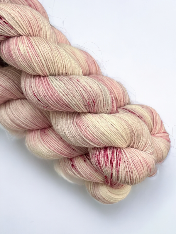 Two skeins of WoolWomen Merino Sock, käsinvärjätty lanka in cream with soft pink and red speckles, are twisted together on a white background, highlighting the beauty of superwash merinovilla.