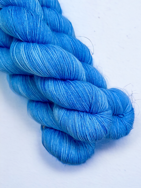 Three skeins of WoolWomen Merino Sock yarn in bright blue are neatly twisted together and displayed on a white background.