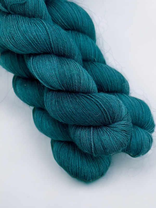 Two skeins of WoolWomen Merino Sock yarn in teal are neatly twisted and stacked on a plain background. The soft, smooth yarn is ideal for knitting or crocheting projects.