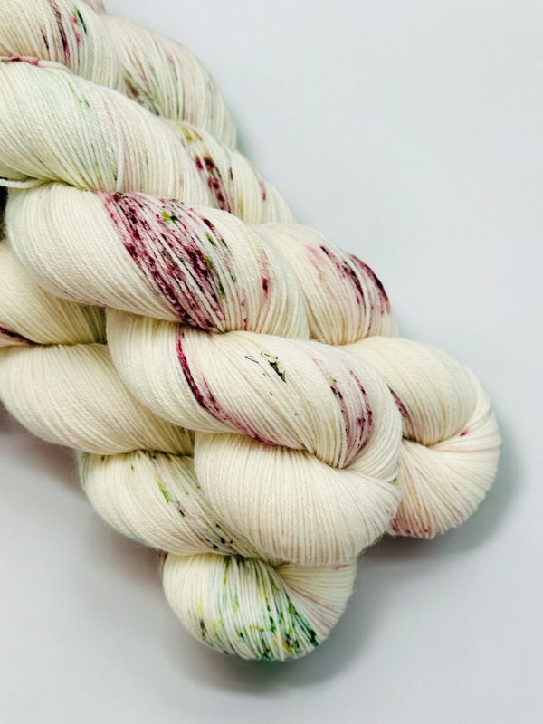 Three skeins of WoolWomen Merino Sock yarn in cream with speckles of pink, burgundy, and green, neatly twisted and displayed on a white background.