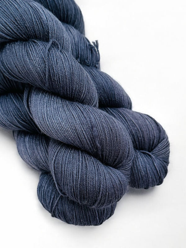 Two neatly twisted skeins of WoolWomen Merino Sock yarn in dark blue are displayed on a white background. The superwash merino wool looks smooth, soft, and subtly lustrous.