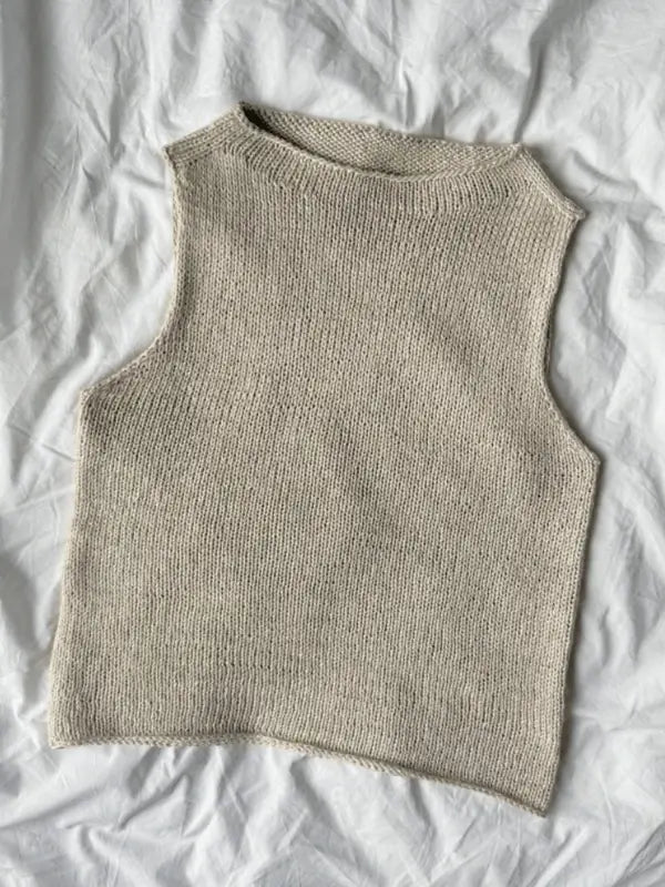 The PetitKnit Ivy Top Neuleohje is a sleeveless, beige knitted top with a simple, minimalistic design, round neckline, and straight armholes—shown laid flat on a white wrinkled fabric background. Perfect for neuleohje suomeksi seekers.