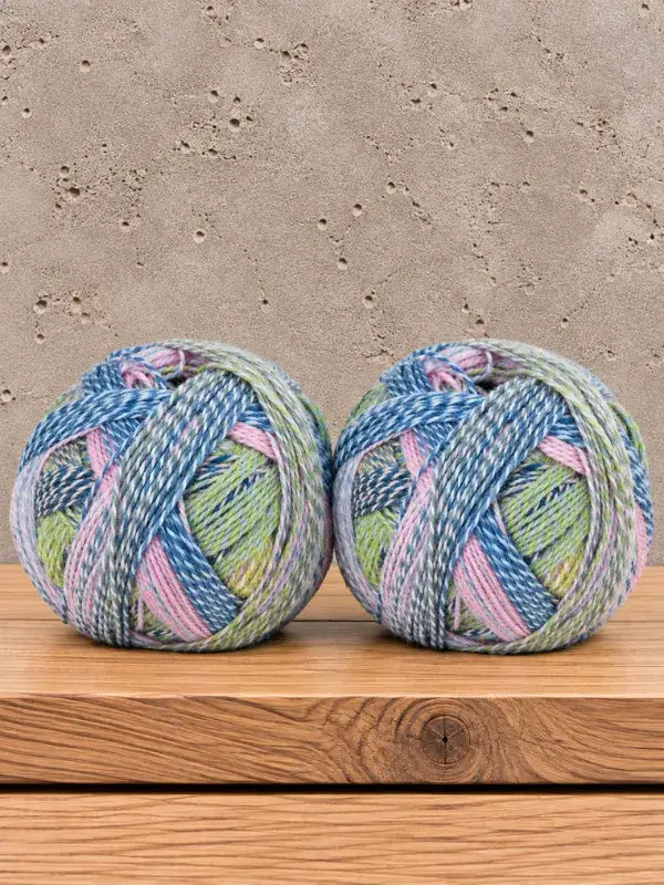 Two round balls of Schoppel-Wolle Edition 3 variegated yarn in shades of blue, green, and pink sitting on a wooden surface.