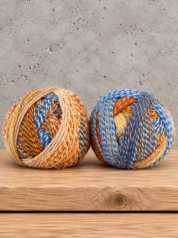 Two balls of Schoppel-Wolle Edition 3 variegated yarn in shades of blue, orange, and tan.