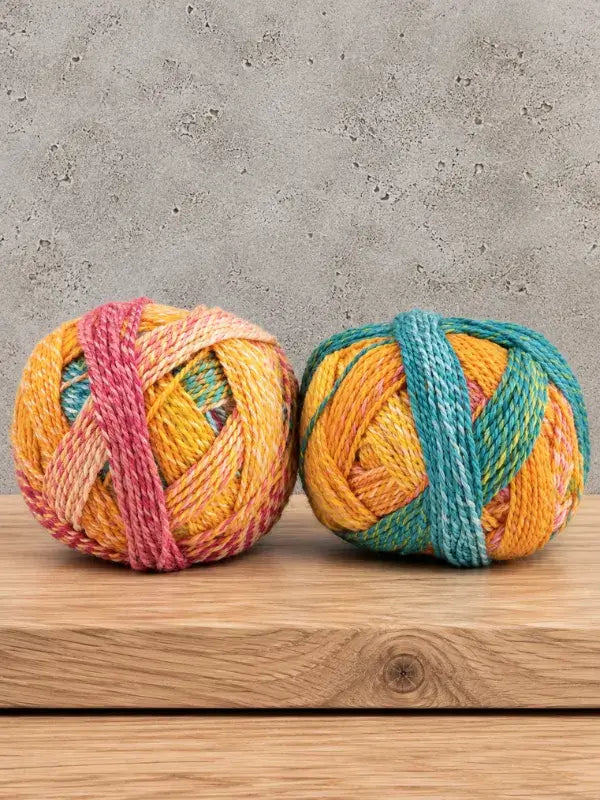 Two balls of Schoppel-Wolle Edition 3 variegated yarn, one featuring pink accents and the other featuring teal accents.