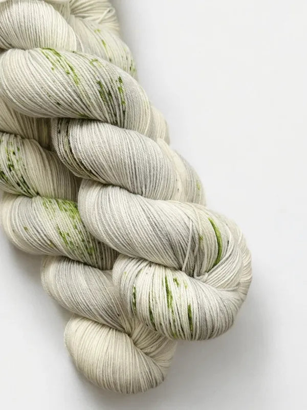 Two skeins of WoolWomen Merino Sock in light gray with subtle green speckles are twisted together and placed on a plain white background.