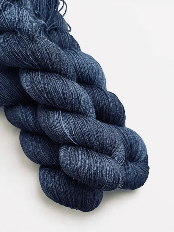 Three skeins of WoolWomen Merino Sock yarn in deep blue are neatly twisted together on a white surface, showing off their soft, smooth texture and subtle sheen.