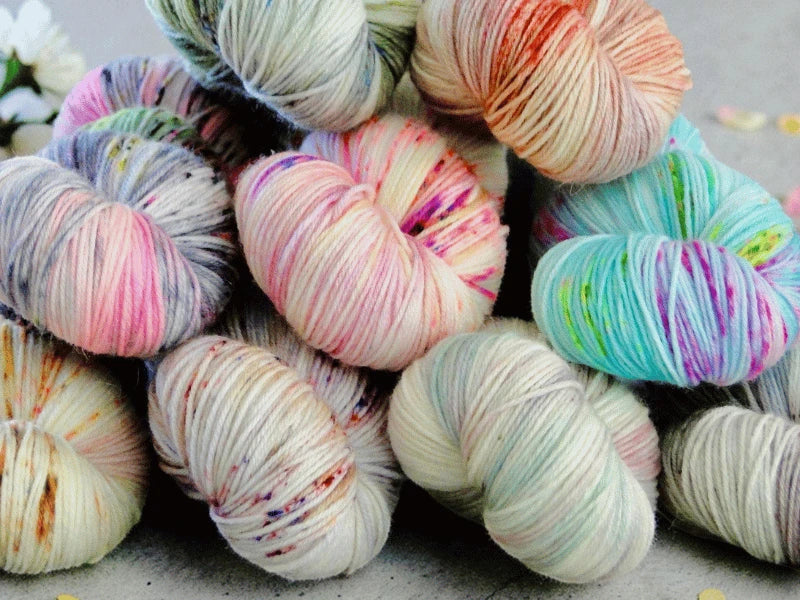 Several skeins of WoolWomen Merino Sock – Yhden Padan Ihme are stacked together, featuring vibrant pink, purple, blue, green, and orange speckles on a light base—perfect mulesing-vapaa merino for your next project.