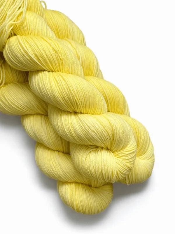 A skein of WoolWomen Merino Sock, soft superwash merinovilla yarn in pale yellow, is neatly twisted against a white background.