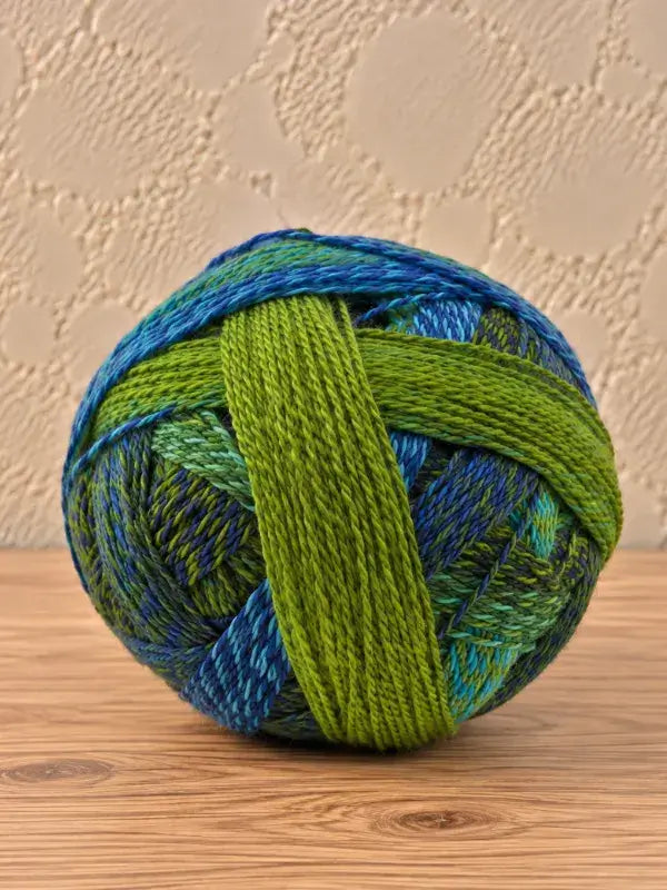 A round ball of Schoppel wolle Zauberball crazy superwash wool yarn in variegated shades of blue and green.