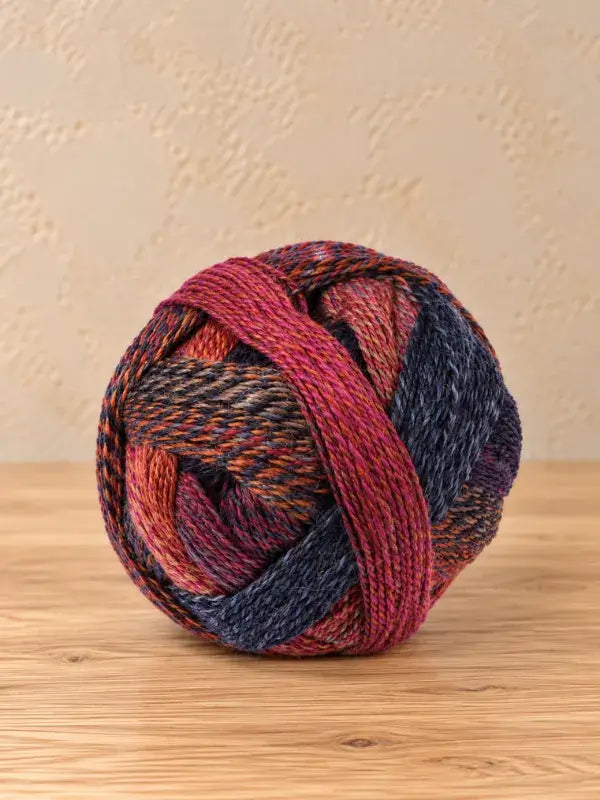 A round ball of Schoppel wolle Zauberball crazy yarn featuring shades of pink, orange, and dark blue.