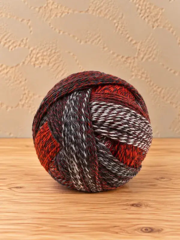 A ball of Schoppel wolle Zauberball crazy variegated yarn featuring striped sections of red, black, grey, and white.