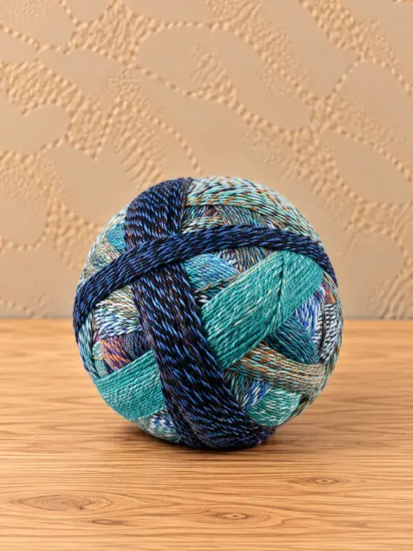 A ball of Schoppel wolle Zauberball crazy yarn in variegated shades of blue, teal, and earth tones.