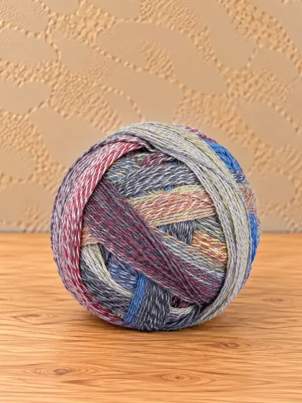 A ball of Schoppel wolle Zauberball crazy yarn featuring multicolored plies in shades of blue, red, yellow, and grey.