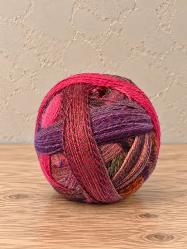 A round ball of Schoppel wolle Zauberball crazy variegated yarn featuring shades of pink, purple, and green.