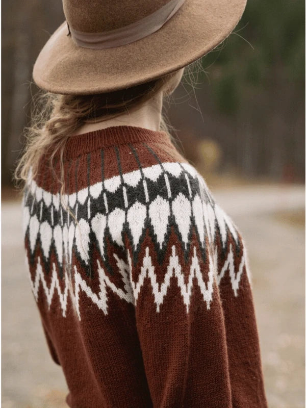 Wearing a brown geometric knit sweater from "Ronja Hakalehto Unfolding Landscapes – 17 Knits for the Road ENG," a person with a loose braid and wide-brimmed hat stands outdoors in Northern Finland style, facing away from the camera.