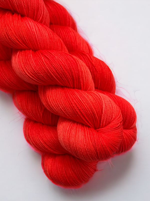 A close-up of two skeins of WoolWomen Merino Sock, a smooth, bright red superwash merinovilla yarn with a soft texture and slight sheen, twisted together on a plain white background.