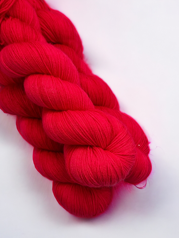 A close-up photo of a skein of bright red WoolWomen Merino Sock yarn, neatly twisted against a plain white background.