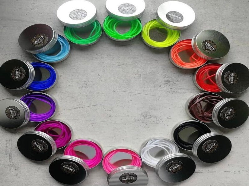 Round arrangement of metal tins, each open to display colorful elastic bands inside. The bands include shades of green, blue, purple, pink, white, black, red, orange, and brown.
