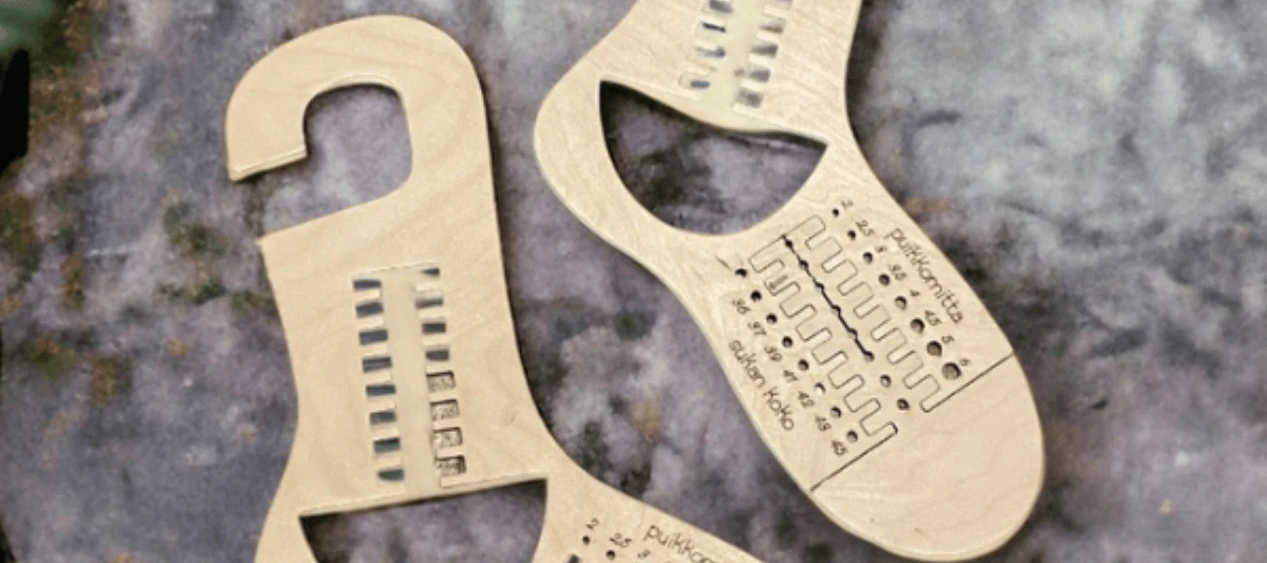 Three wooden sock blockers with measurement holes and engraved text are placed on a textured surface, possibly stone. Each sock blocker has a hook at one end and size markings.