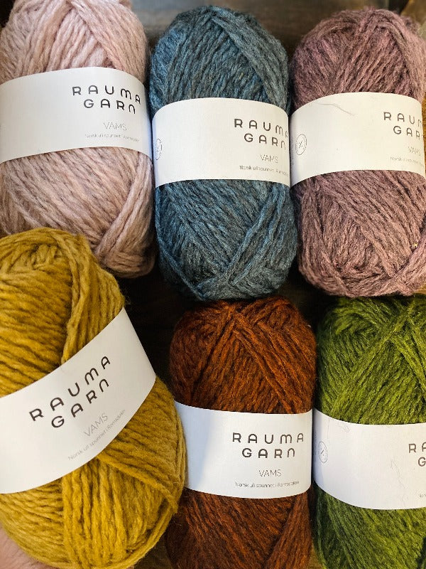 Six skeins of Rauma Garn Vams yarn in various colors, including pink, blue, purple, yellow, orange, and green, arranged in two rows on a wooden surface.