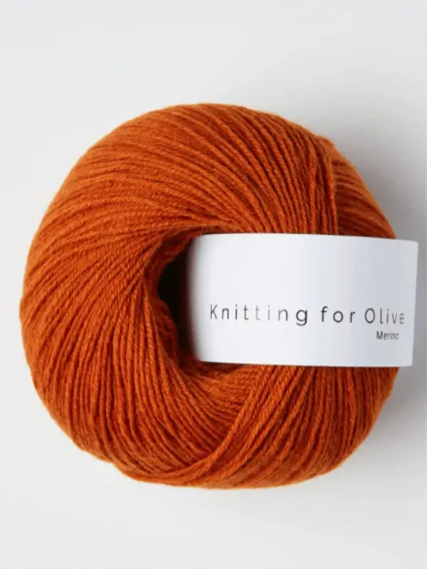 A ball of Knitting for Olive Merino yarn in burnt orange with a white "Knitting for Olive" label, displayed against a white background.