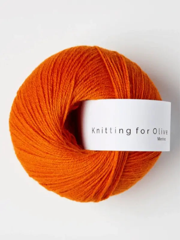 A bright orange ball of Knitting for Olive Merino yarn with a white label that reads "Knitting for Olive Merino, Öko-Tex sertifioitu.