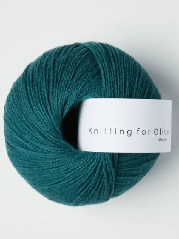 A ball of teal Knitting for Olive Merino yarn with a white label, Öko-Tex certified, is set against a light background.