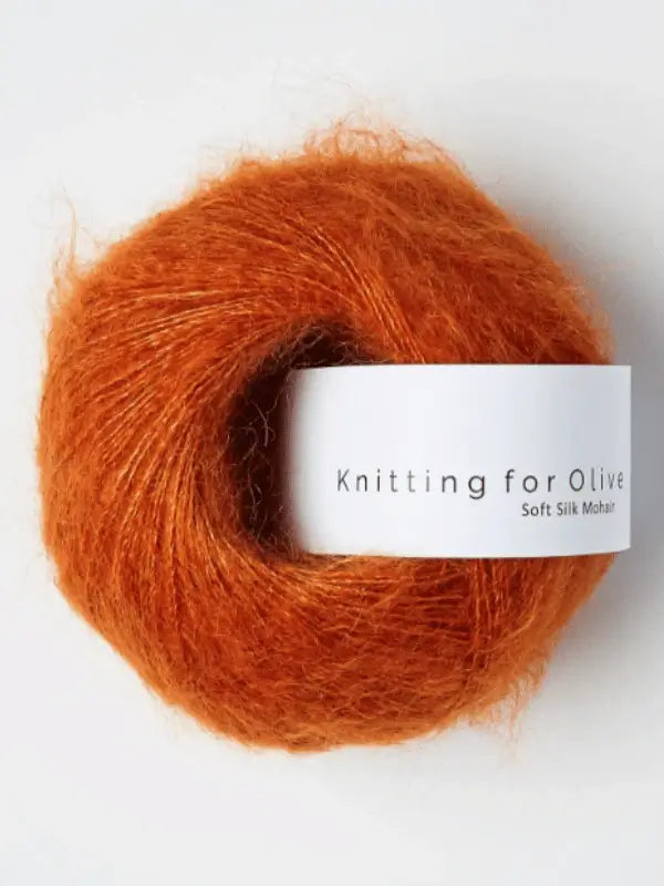 A skein of Knitting for Olive Soft Silk Mohair in a soft orange hue, wrapped with a white paper label, spun from fine kid mohair and certified by the Responsible Mohair Standard for ethical sourcing. This luxurious yarn is ideal for delicate knitting projects.