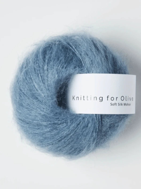 A skein of fluffy, blue yarn labeled Knitting for Olive Soft Silk Mohair rests on a white background. This yarn is made from responsibly produced mohair—making it a luxurious kid mohair option that's perfect for your next project.
