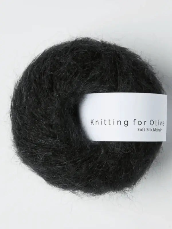A ball of dark gray Knitting for Olive Soft Silk Mohair yarn with a white label bearing the product name, set against a plain light background.