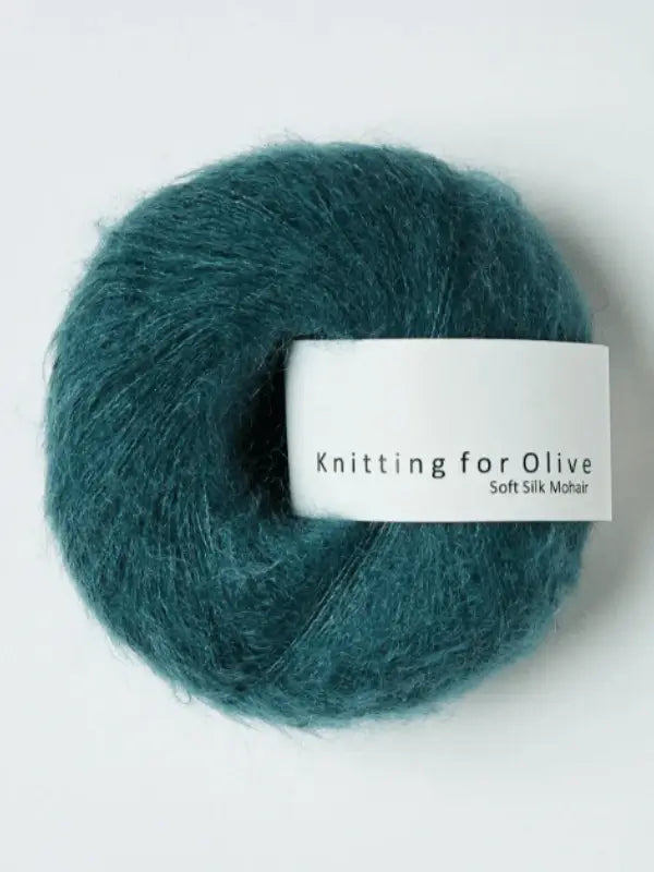 A skein of Knitting for Olive Soft Silk Mohair yarn in a teal shade, made from responsible mohair and silk fibers, is displayed against a plain white background.