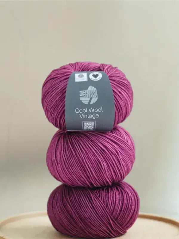 Three stacked balls of deep magenta Lana Grossa Cool wool vintage merino wool yarn.