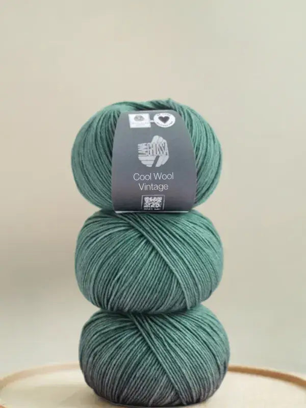 Three stacked balls of forest green Lana Grossa Cool wool vintage yarn with a product label on the top ball.