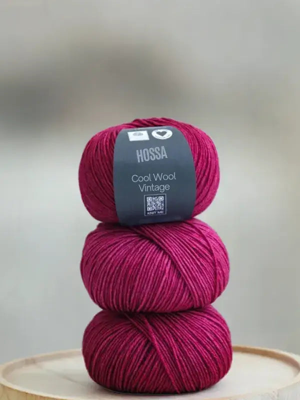Three stacked balls of deep magenta Lana Grossa Cool wool vintage yarn, with a label on the top ball.